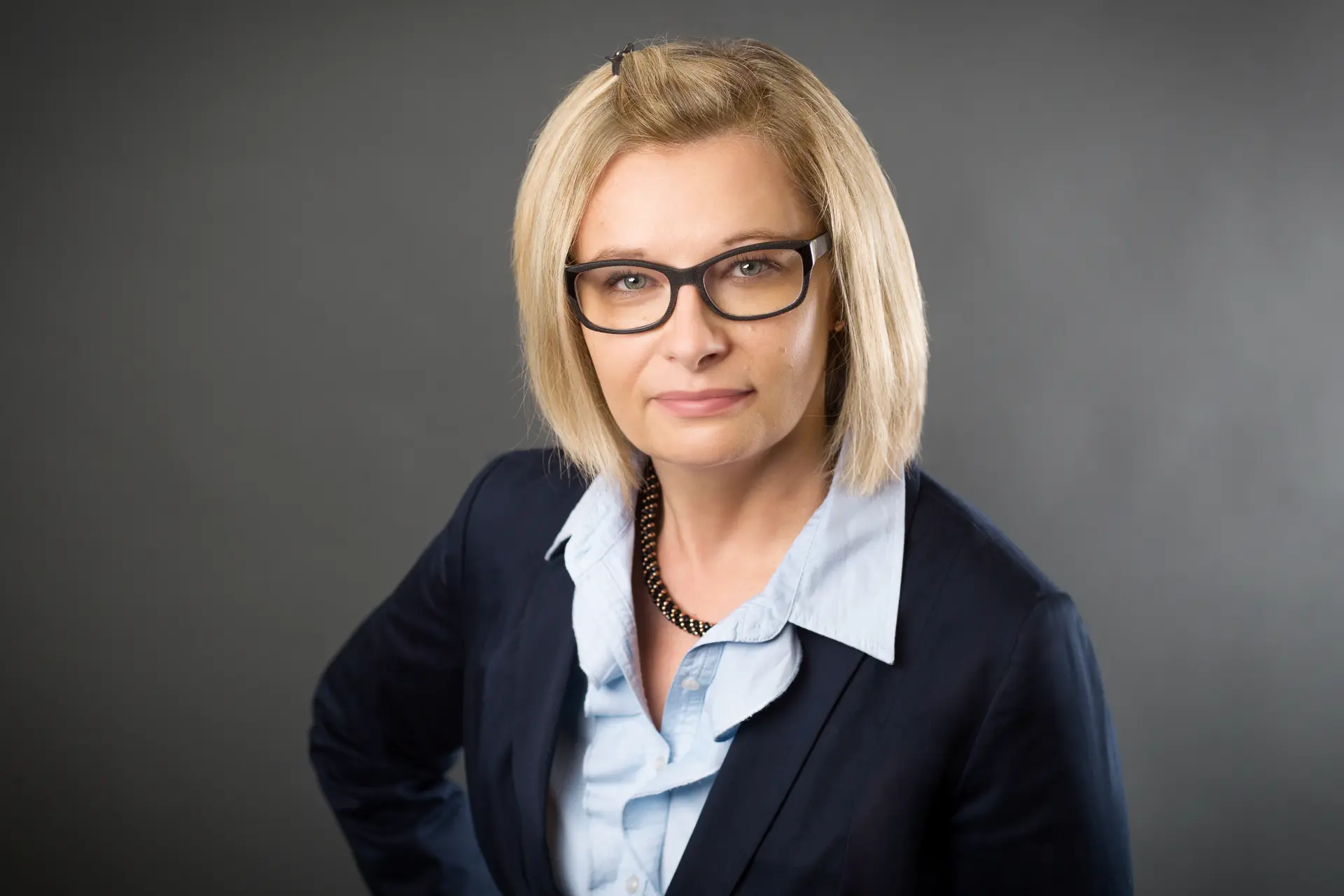 Beate Bania, Assistenz der Geschäftsführung der Witzleben AG, mit Brille und dunklem Blazer vor grauem Hintergrund