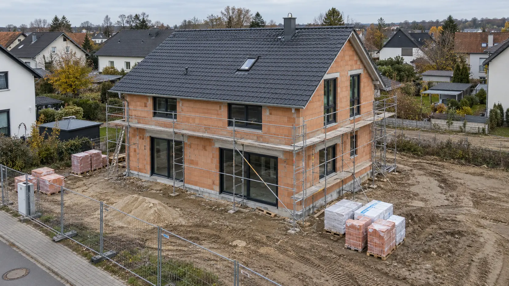 Baustelle eines Einfamilienhauses im Rohbau mit Gerüst und Baumaterial, von oben