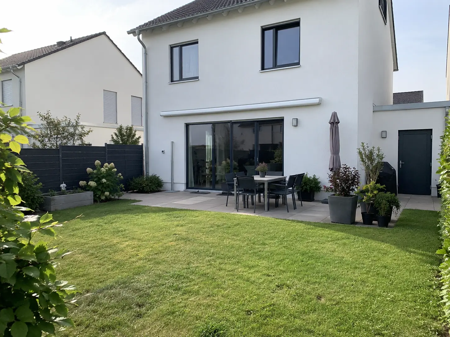 Haus mit großer Fensterfront zur Terrasse, davor ein gepflegter Rasen