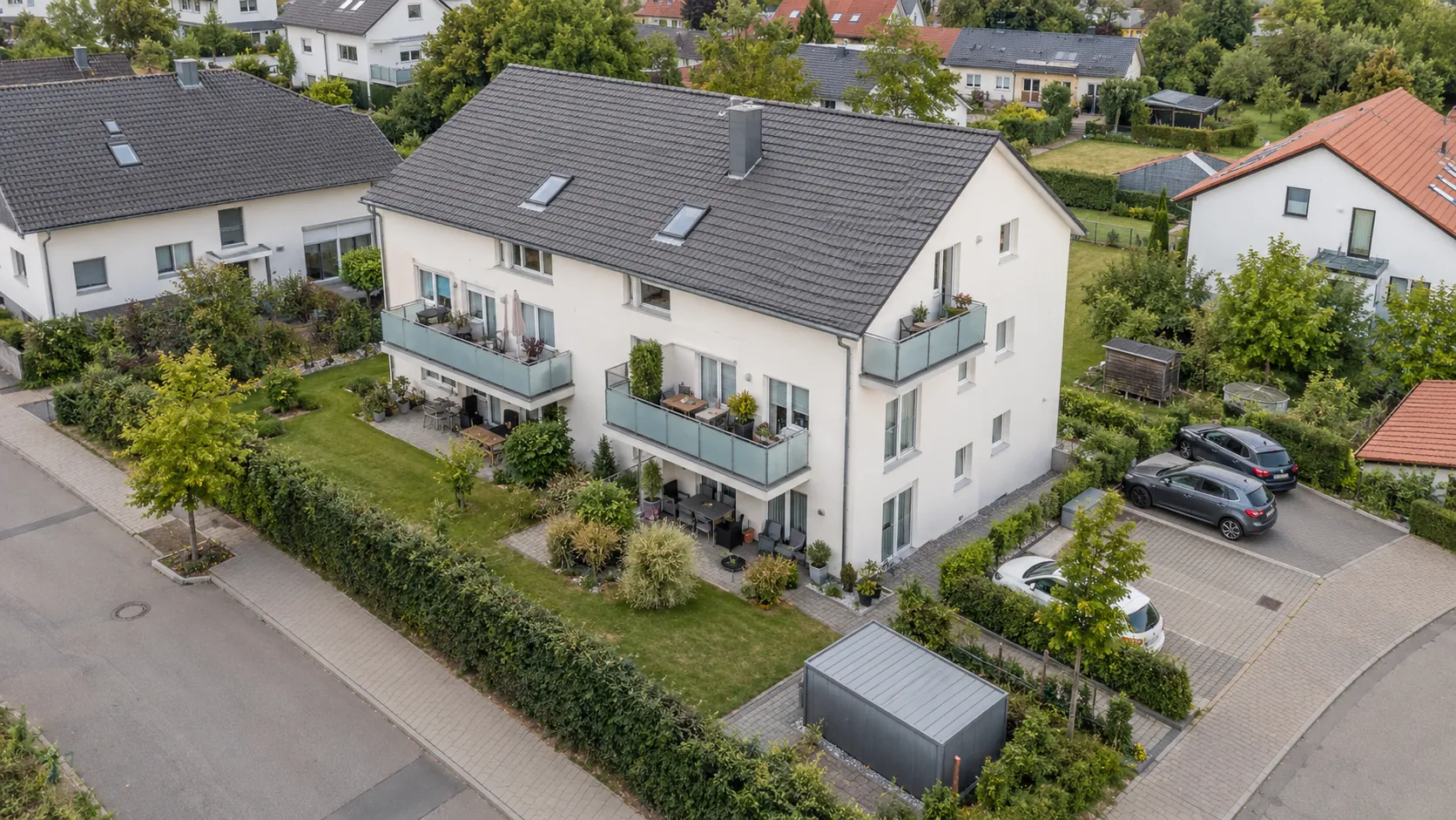 Mehrfamilienhaus mit Balkonen, Gärten und Stellplätzen in einer grünen Wohnstraße, von oben