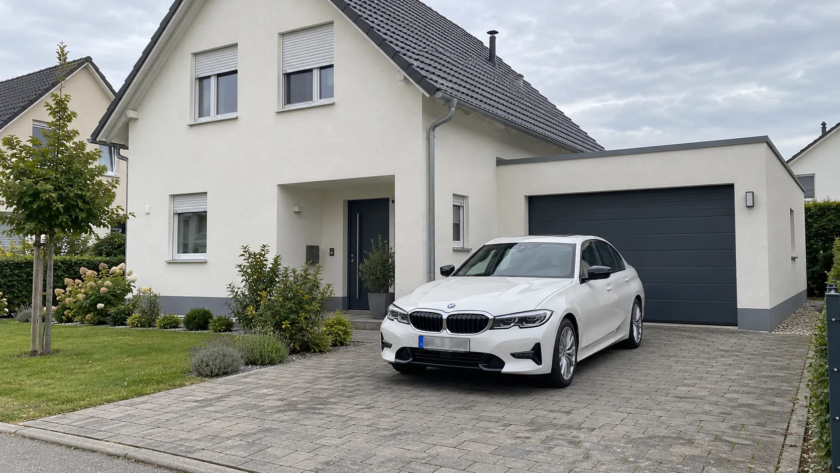 Weißes Auto in der gepflasterten Einfahrt vor einem Einfamilienhaus mit Garage