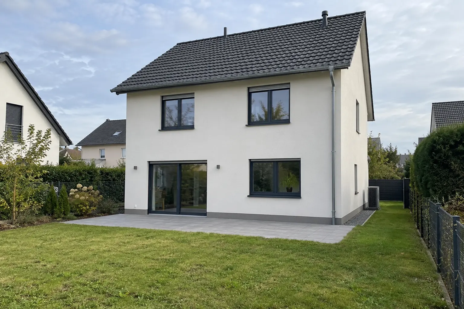 Einfamilienhaus mit dunklem Satteldach und Glastür zur Terrasse, davor der Rasen