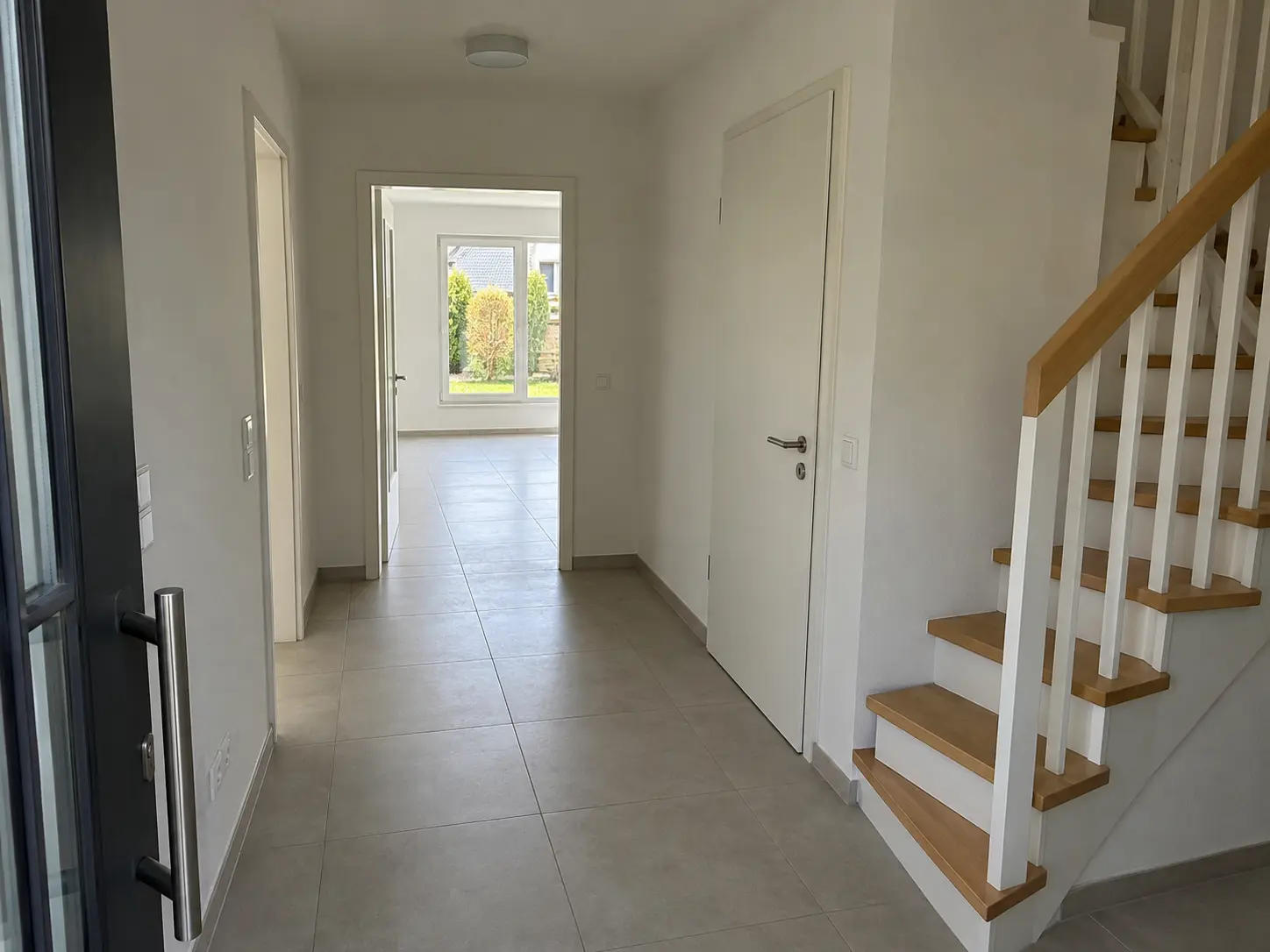 Heller Eingangsflur mit Holztreppe und Blick bis in den Garten