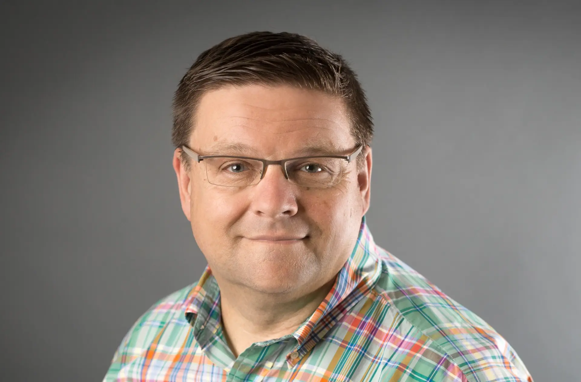 Volker von Witzleben, Vorstand der Witzleben AG, lächelnd mit Brille und kariertem Hemd vor grauem Hintergrund